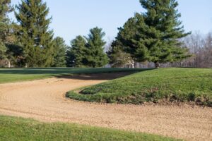 A well-groomed sand bunker with trees in the background.