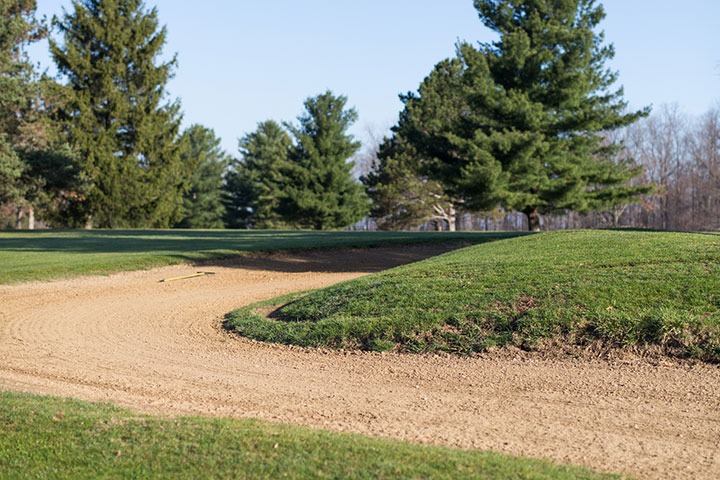 A well-groomed sand bunker with trees in the background.