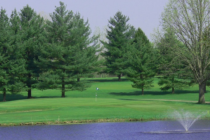 View of fountain and lake with green and flag in the background.