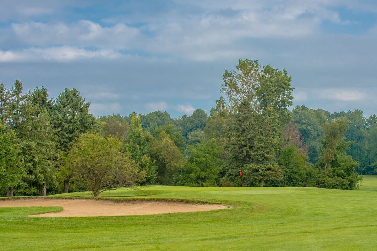 View of a bunker and green just beyond with dense wood coverage in the background.